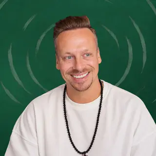 Fabian Henzler in a white shirt with mala beads, smiling straight into the camera, in front of forest green with drawn rings